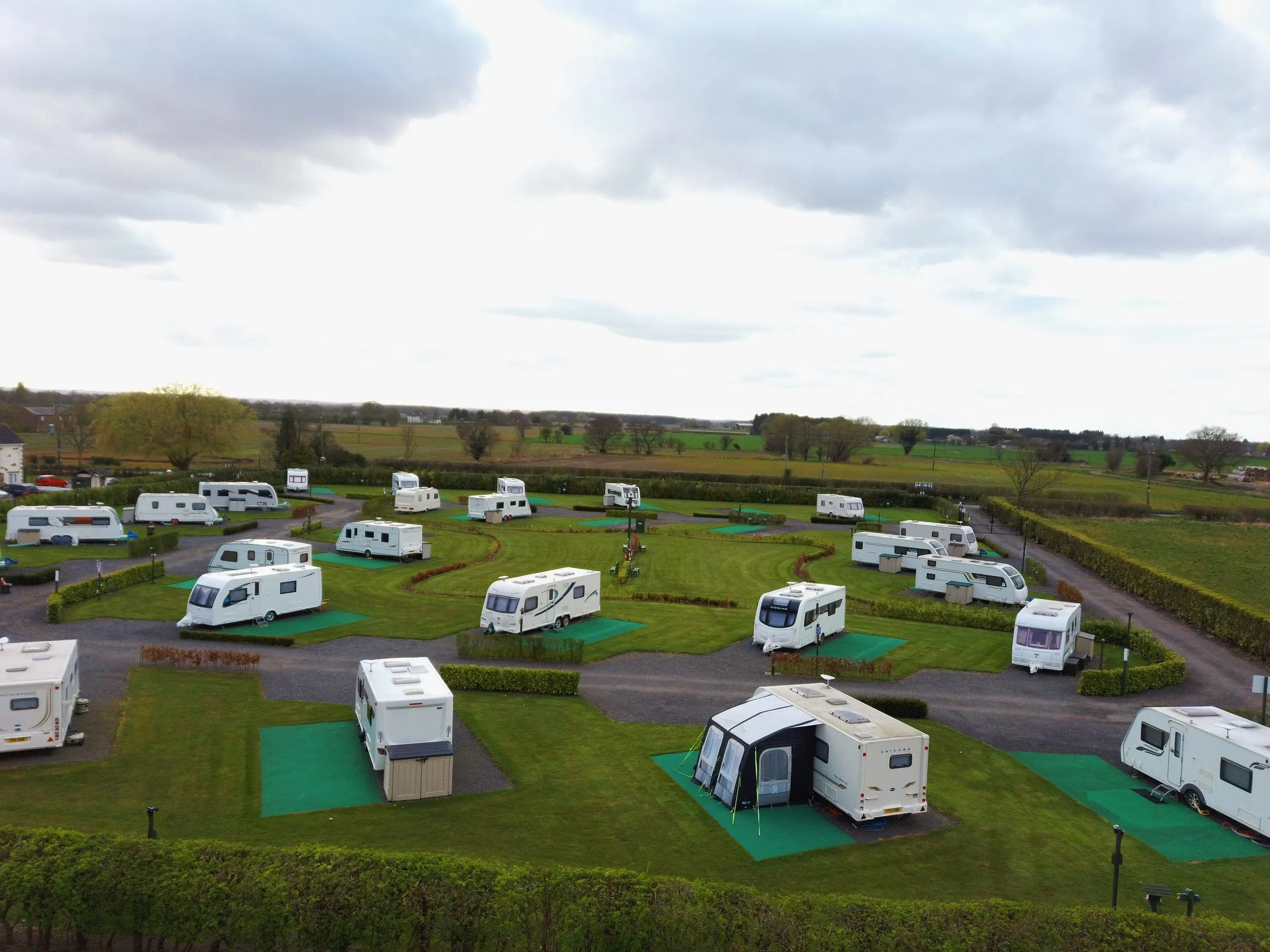 Aerial view of the front field with caravans on hard-standing pitches and green awning bases